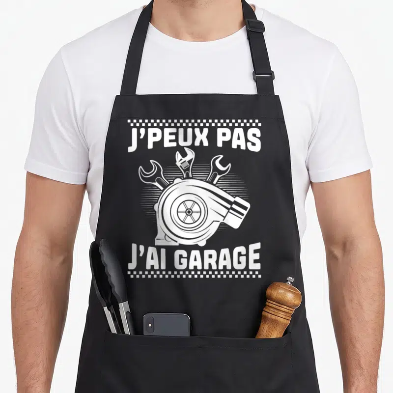 Tablier de cuisine noir avec un turbo blanc, des clés anglaises et le texte J'peux pas j'ai garage en typographie épaisse.
