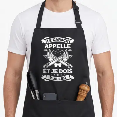 Tablier de cuisine noir avec deux clés à molette croisées et l'inscription Le garage appelle et je dois y aller en typographie blanche vintage.