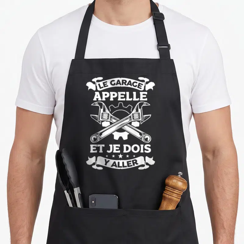 Tablier de cuisine noir avec deux clés à molette croisées et l'inscription Le garage appelle et je dois y aller en typographie blanche vintage.
