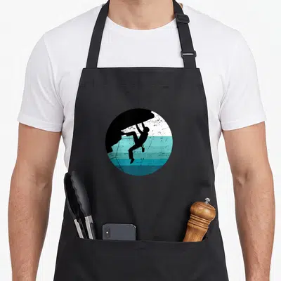 Tablier de cuisine noir avec illustration circulaire d'un alpiniste escaladant une paroi bleue et blanche.