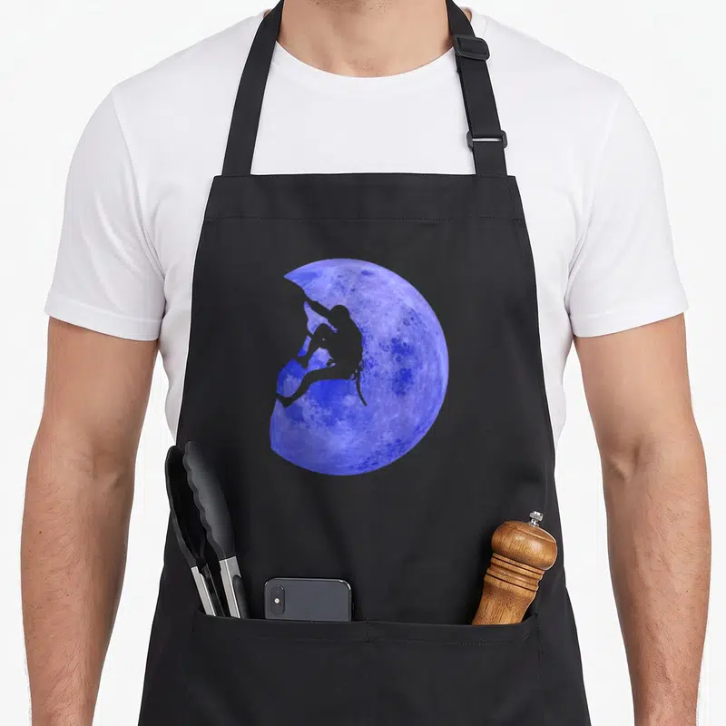 Tablier de cuisine noir avec une lune bleue texturée et une silhouette grise d'escaladeur en train de grimper sur le bord.