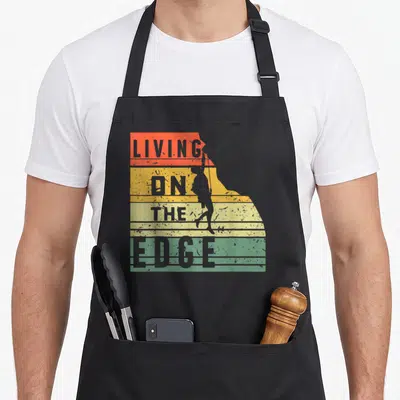 Tablier de cuisine noir avec inscription Living on the Edge et silhouette d'alpiniste sur fond dégradé vintage.