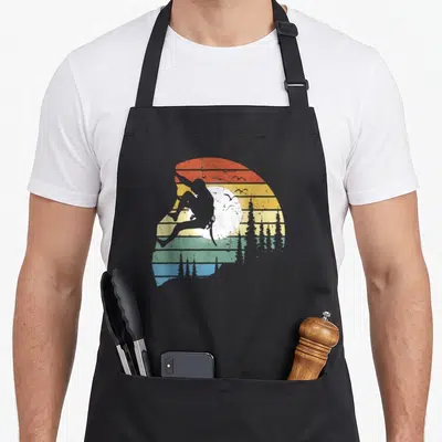 Tablier de cuisine noir avec silhouette de grimpeur sur fond rayé vintage coloré et arbres.