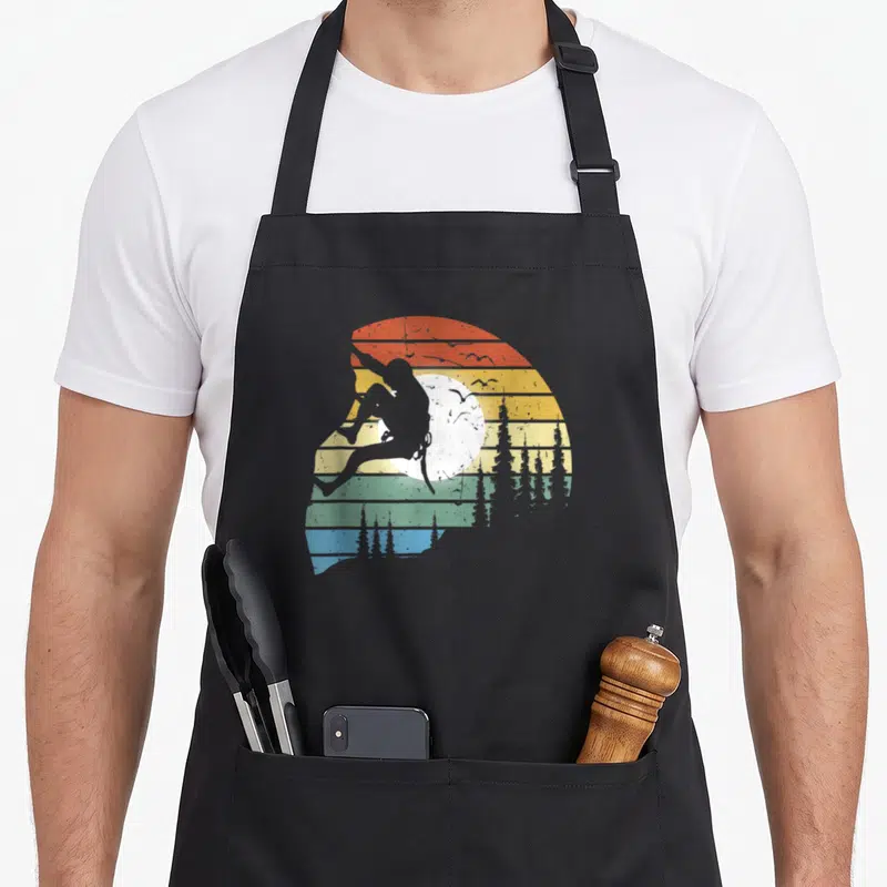Tablier de cuisine noir avec silhouette de grimpeur sur fond rayé vintage coloré et arbres.