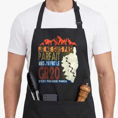 Tablier de cuisine noir avec illustration du GR20, silhouette de Corse et texte humoristique en orange et bleu.