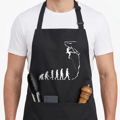 Tablier de cuisine noir avec une illustration blanche représentant l'évolution humaine se terminant par un grimpeur sur une paroi de blocage.