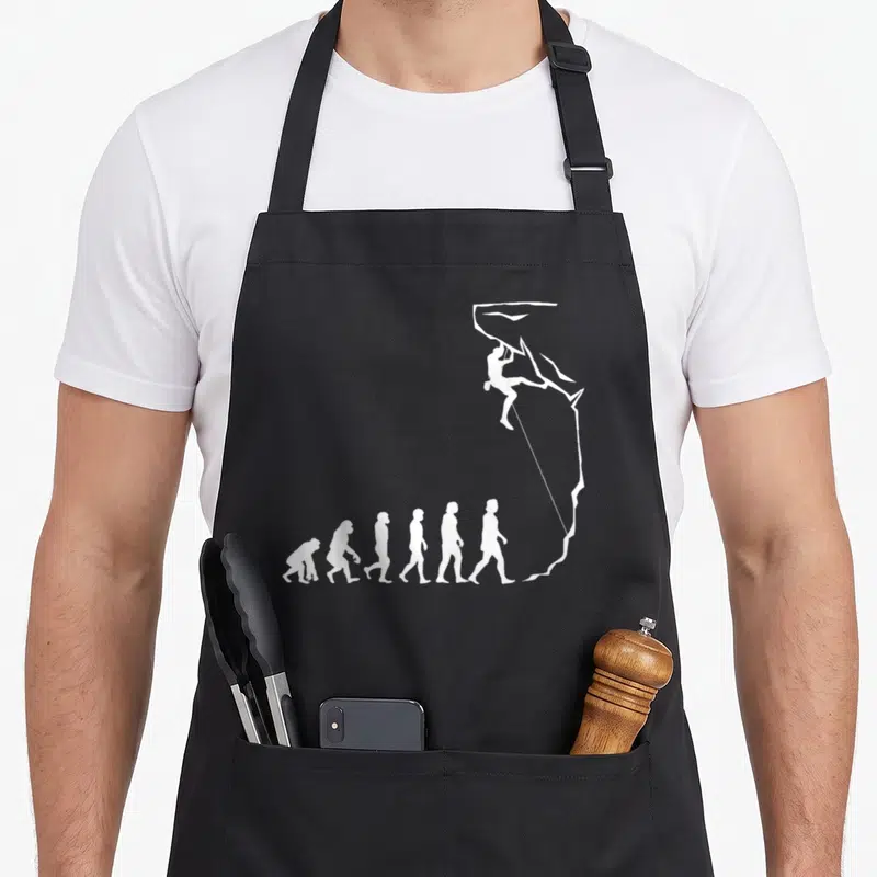 Tablier de cuisine noir avec une illustration blanche représentant l'évolution humaine se terminant par un grimpeur sur une paroi de blocage.