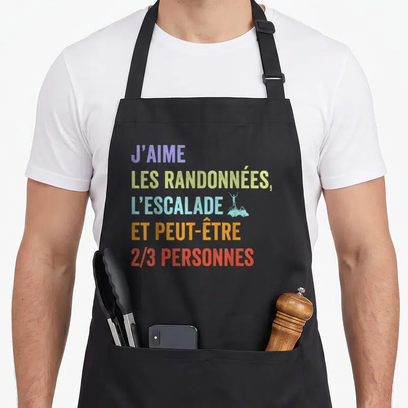 Tablier de cuisine noir avec texte coloré J'aime les randonnées l'escalade et peut-être 2/3 personnes illustré d'un grimpeur sur un sommet.