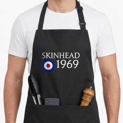 Tablier de cuisine noir avec le texte Skinhead 1969 et un emblème circulaire rouge blanc et bleu au centre.