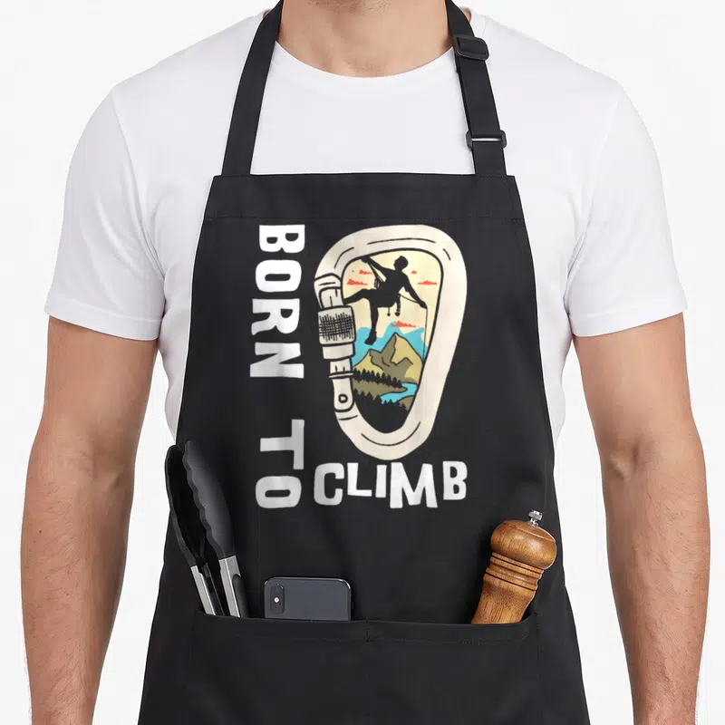 Tablier de cuisine noir avec illustration mousqueton vintage, silhouette grimpeur et texte Born To Climb vertical.