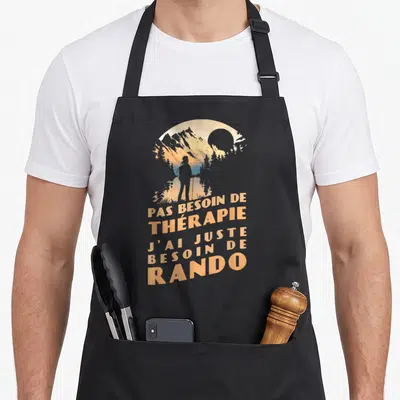 Tablier de cuisine noir avec silhouette de randonneur et texte orange sur fond de montagnes