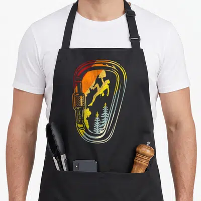 Tablier de cuisine noir avec illustration vintage d'un mousqueton contenant un silhouetté de grimpeur et deux arbres conifères bleus.