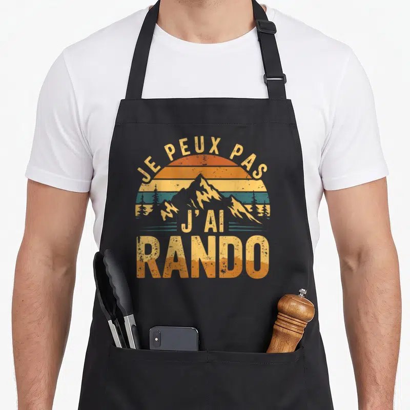 Tablier de cuisine noir avec illustration vintage d'un soleil couchant sur un massif montagneux et le texte Je peux pas j'ai rando.