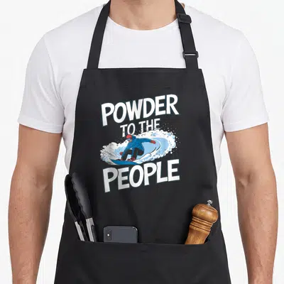 Tablier de cuisine noir avec illustration d'un snowboarder et le texte « Powder to the People » en grosses lettres blanches.