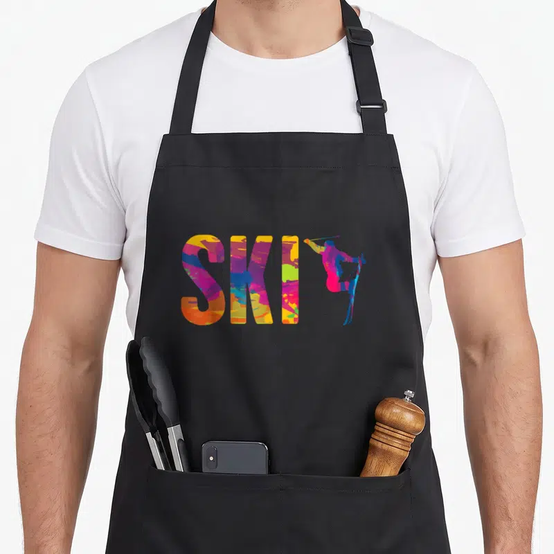 Tablier de cuisine noir avec le mot SKI en couleurs vives et une silhouette de skieur en action sur la droite.