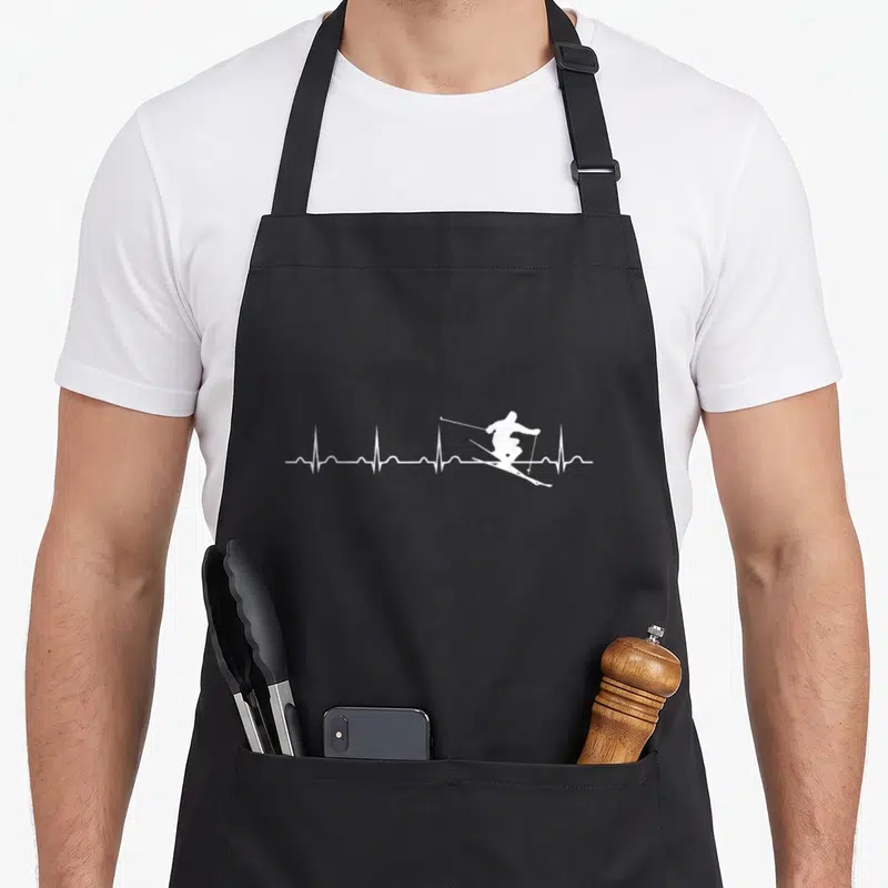 Tablier de cuisine noir avec un motif blanc représentant une ligne d'EKG traversée par la silhouette d'un skieur en pleine descente.