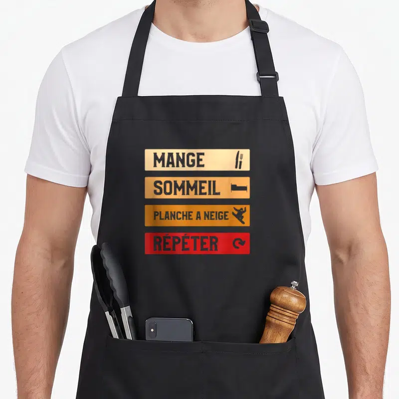 Tablier de cuisine noir avec quatre bandes colorées affichant les mots Mange, Sommeil, Planche à Neige et Répéter accompagnés d'icônes.