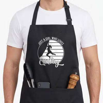 Tablier de cuisine noir avec silhouette d'escaladeuse et texte blanc Just a girl who loves climbing dans un motif circulaire.