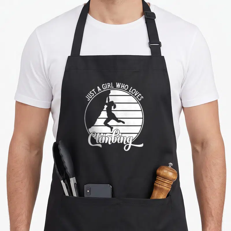 Tablier de cuisine noir avec silhouette d'escaladeuse et texte blanc Just a girl who loves climbing dans un motif circulaire.