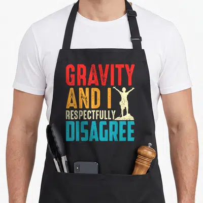 Tablier de cuisine noir avec texte multicolore et silhouette d'escaladeur sur sommet rocheux.