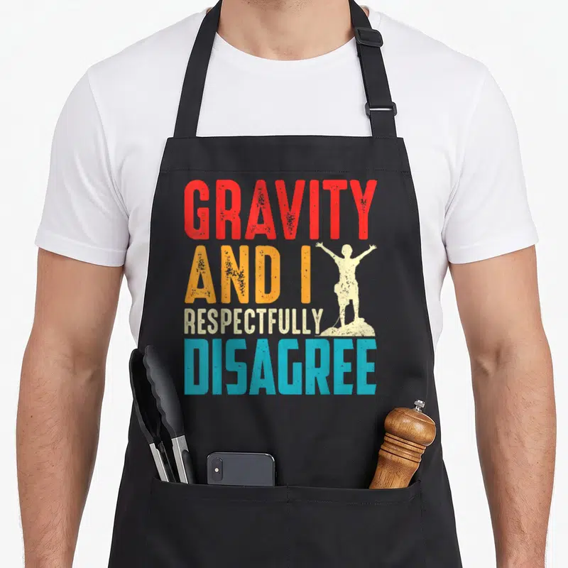 Tablier de cuisine noir avec texte multicolore et silhouette d'escaladeur sur sommet rocheux.