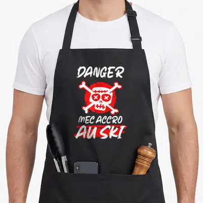 Tablier de cuisine noir avec un crâne rouge et l'inscription Danger Mec Accro Au ski en lettres blanches.