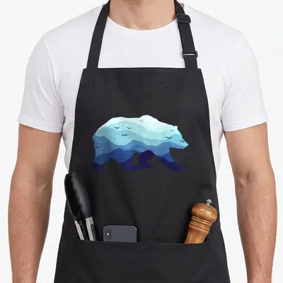 Tablier de cuisine noir avec une illustration d'ours formée par des reliefs montagneux bleus et des oiseaux en vol.