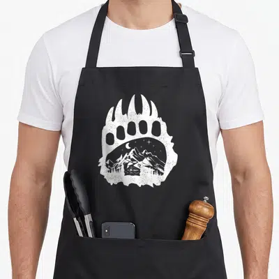 Tablier de cuisine noir avec une grande patte d'ours blanche contenant un paysage de montagne avec tente et étoiles.