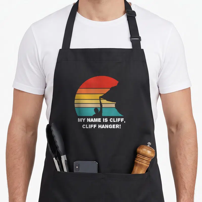 Tablier de cuisine noir avec motif escalade vintage et texte My Name Is Cliff, Cliff Hanger en blanc.