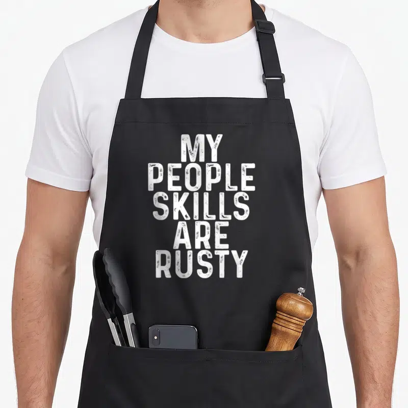 Tablier de cuisine noir avec le texte blanc « Mes compétences sociales sont rouillées » en typographie usée.