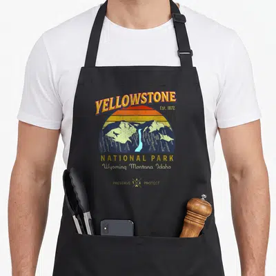 Tablier de cuisine noir avec illustration vintage Yellowstone National Park et paysage montagneux aux couleurs chaudes.