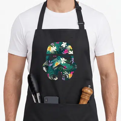 Tablier de cuisine noir avec silhouette de casque de Stormtrooper remplie de fleurs et de feuilles tropicales colorées.