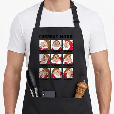 Tablier de cuisine noir avec neuf illustrations des sept nains et le texte GRUMPY en grille.