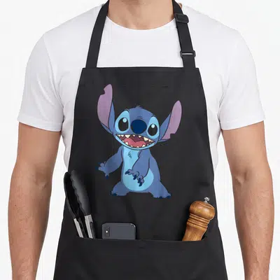 Tablier de cuisine noir avec Stitch debout, grand sourire et grandes oreilles violettes.