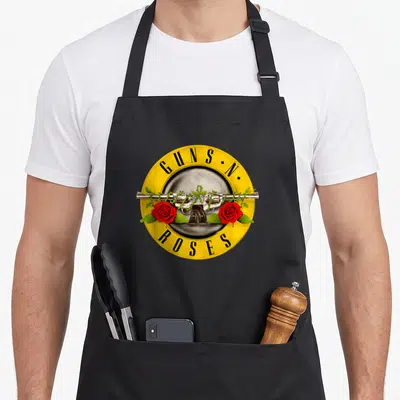 Tablier de cuisine noir avec logo Guns N Roses, revolver et roses rouges sur fond jaune circulaire.