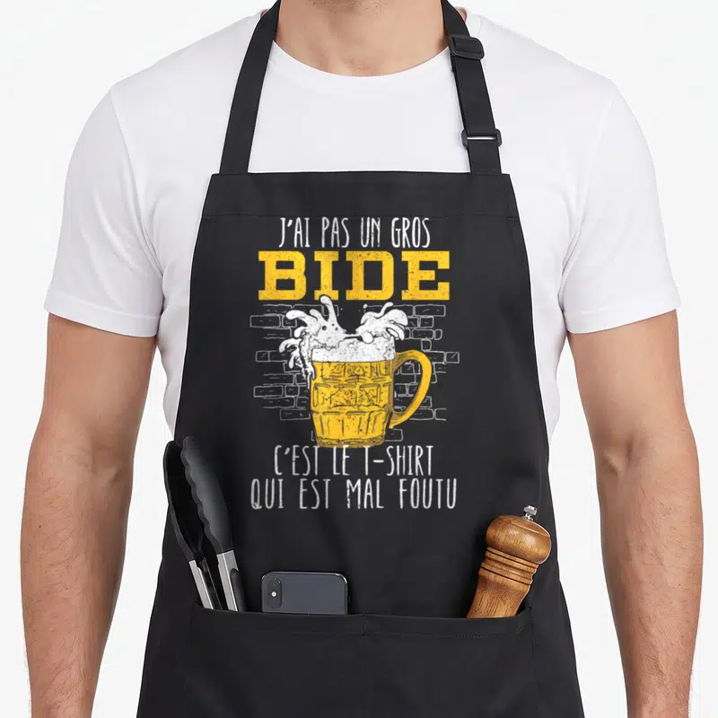 Tablier de cuisine noir avec une illustration de grande bière et la phrase J'ai pas un gros bide c'est le « t-shirt » qui est mal foutu imprimée en jaune et blanc.