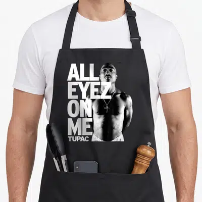 Tablier de cuisine noir avec portrait de Tupac et texte All Eyez On Me en grosses lettres blanches.