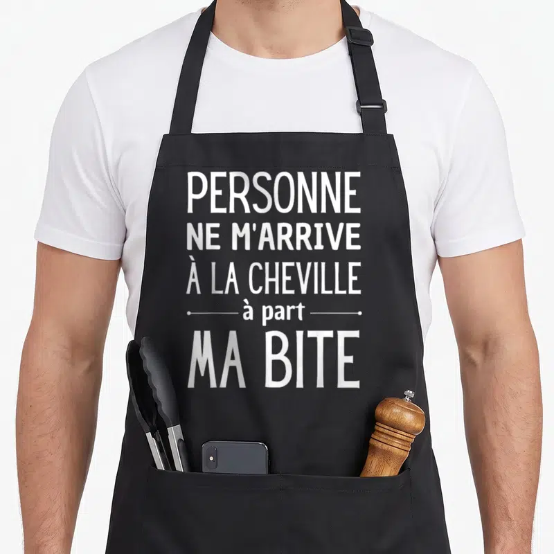 Tablier de cuisine noir avec inscription Personne ne m'arrive à la cheville à part ma bite en lettres blanches capitales.