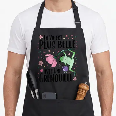 Tablier de cuisine noir avec une illustration de grenouille verte tenant une fleur rose et le texte La vie est plus belle avec une grenouille.