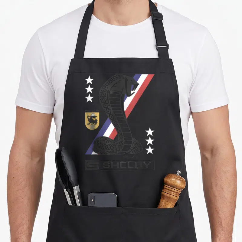 Tablier de cuisine noir avec un cobra géométrique, bandes rouges bleues blanches, six étoiles et le logo Shelby en bas.