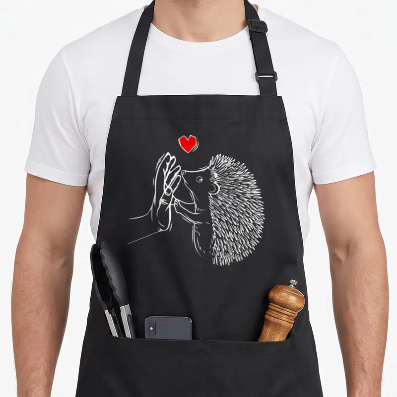 Tablier de cuisine noir avec illustration d'un hérisson blanc tenant une main sous un cœur rouge vif.