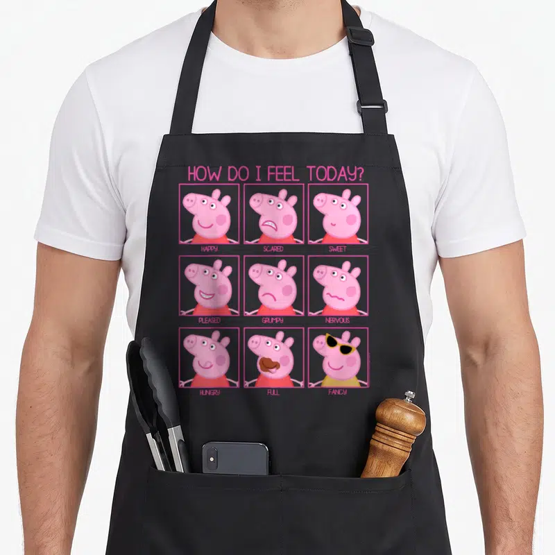 Tablier de cuisine noir avec grille de neuf visages de Peppa Pig illustrant des émotions comme happy, angry ou hungry.