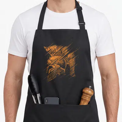 Tablier de cuisine noir avec illustration orange d'un casque de guerrier spartan aux traits dynamiques et texture pointilliste.