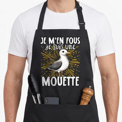 Tablier de cuisine noir avec illustration de mouette blanche et grise, texte blanc et rayons jaunes en arrière-plan.