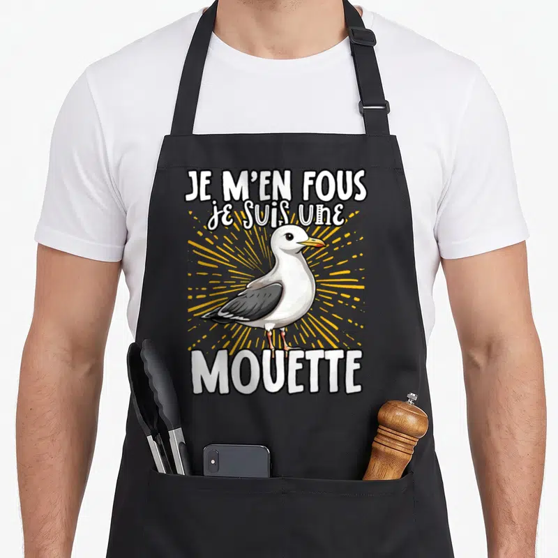 Tablier de cuisine noir avec illustration de mouette blanche et grise, texte blanc et rayons jaunes en arrière-plan.