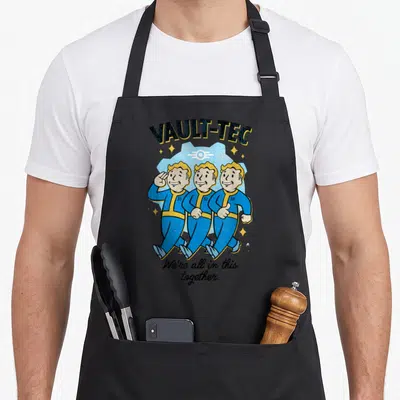 Tablier de cuisine noir avec illustration Vault-Tec montrant trois personnages en combinaisons bleues marchant ensemble sous un logo rétro.