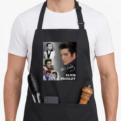 Tablier de cuisine noir avec collage de portraits d'Elvis Presley, signature et nom imprimé en blanc.