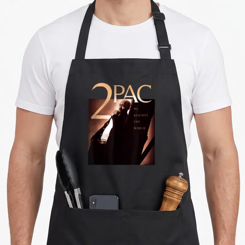 Tablier de cuisine noir avec le portrait de 2PAC et le texte 2PAC Me Against The World imprimé en doré.