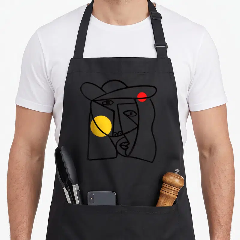 Tablier de cuisine noir avec un portrait abstrait aux traits géométriques et cercles jaune et rouge.