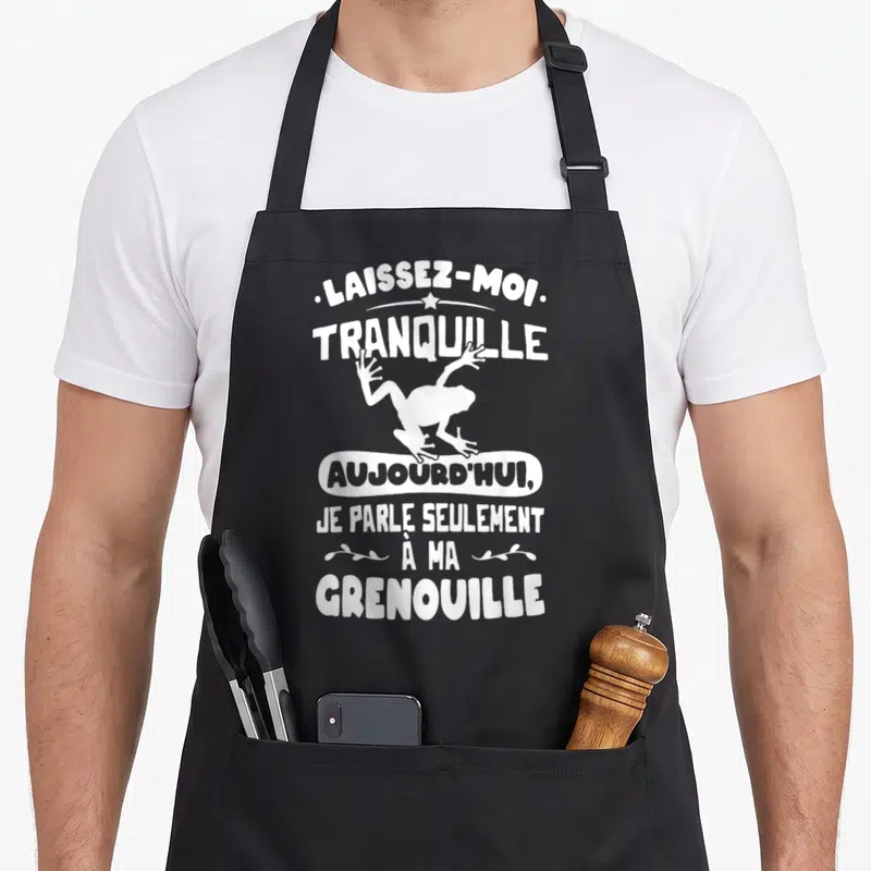 Tablier de cuisine noir avec silhouette blanche de grenouille et texte humoristique en typographie manuscrite.